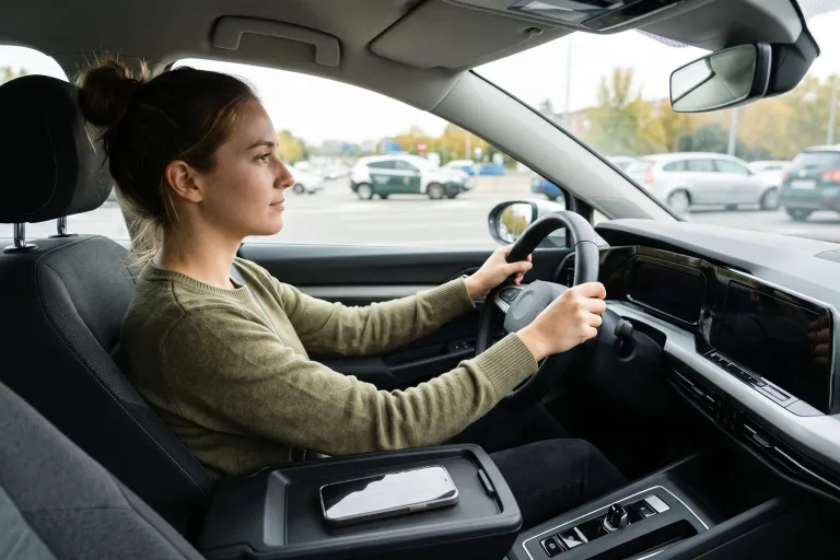 Conductora atenta a la carretera con las dos manos en el volante y el móvil apartado en la consola central
