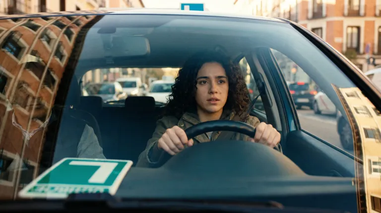 Persona joven preparándose para el examen práctico de conducir, revisando documentación junto al coche de autoescuela