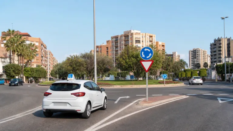 Coche de autoescuela circulando por una glorieta urbana similar a las zonas de examen práctico en Murcia